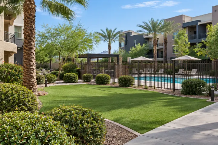 Apartment community courtyard with trimmed shrubs, palms, turf and a pool fence, well maintained