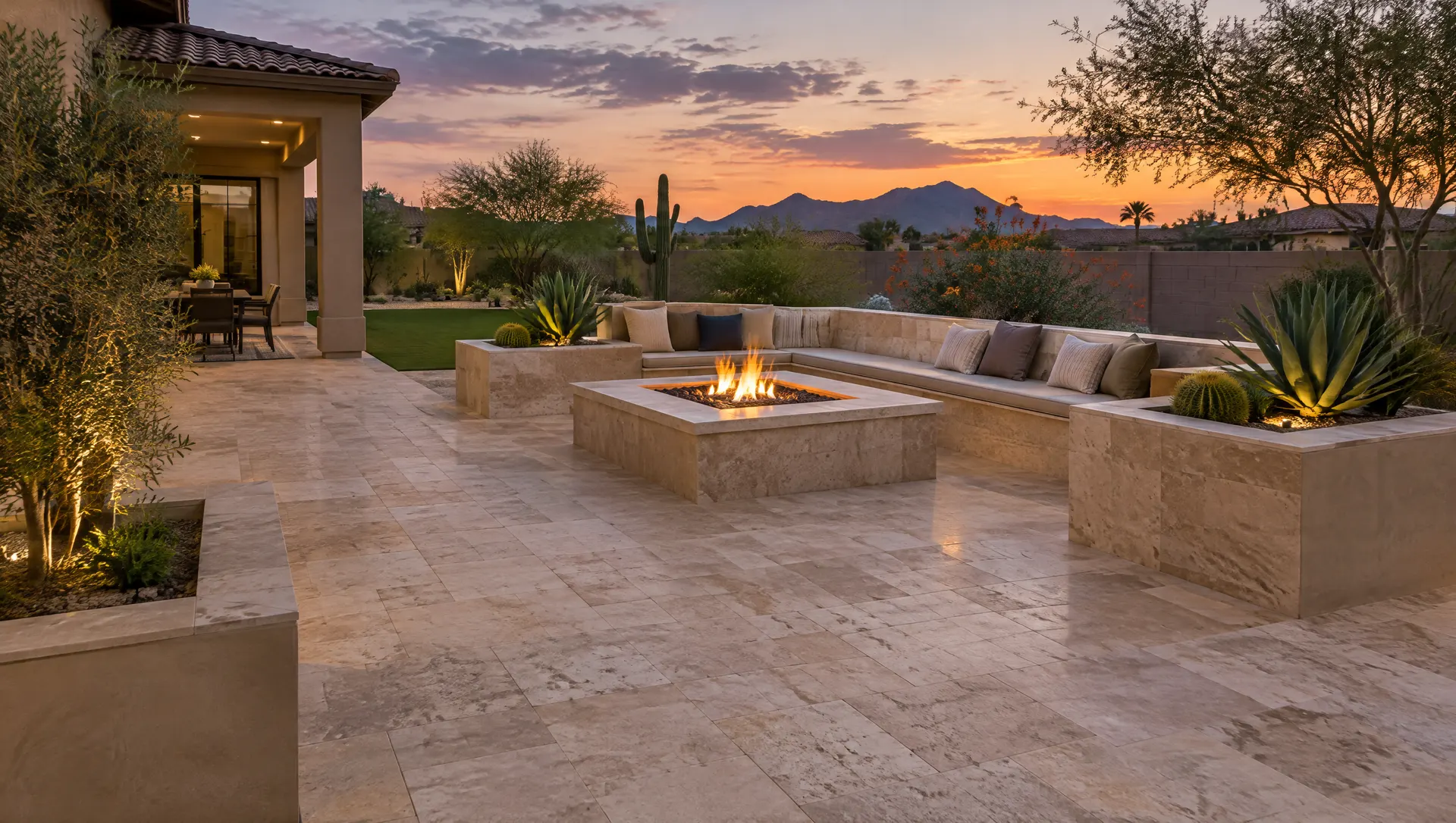 Large travertine-color paver patio with a seat wall, fire pit and built-in planters in an Arizona backyard at dusk